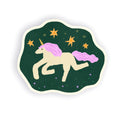 A die-cut sticker featuring a whimsical illustration of a cream-colored unicorn with a pink mane and tail, set against a dark green background with yellow stars.